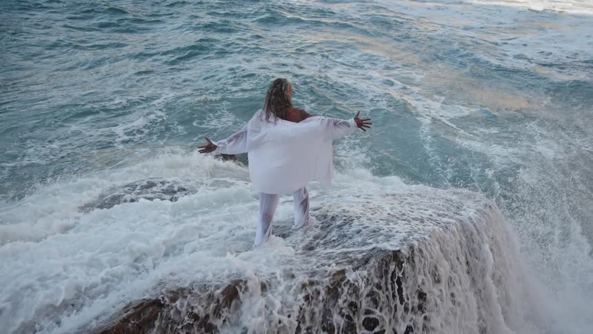 The man stretches his arms out as waves hit his legs