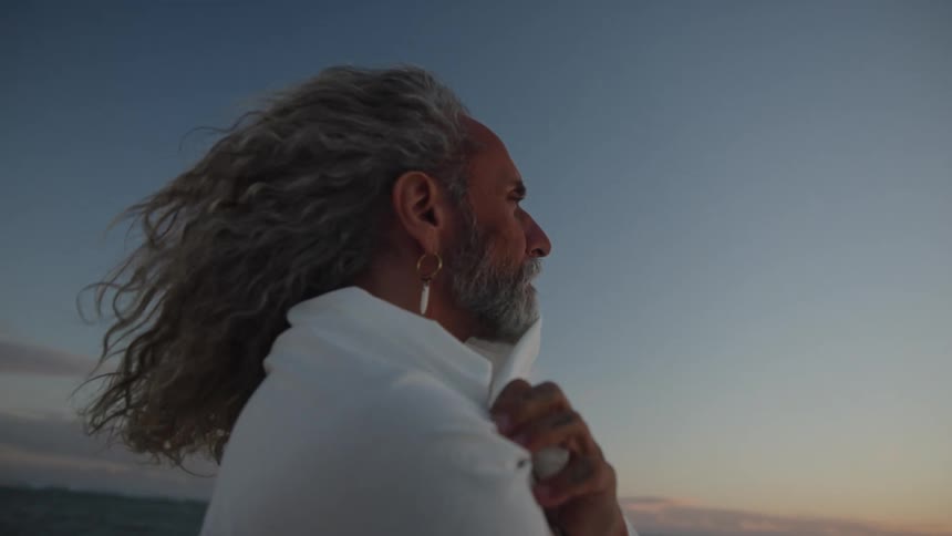 Grayhaired man looking at the horizon by the sea with the wind blowing