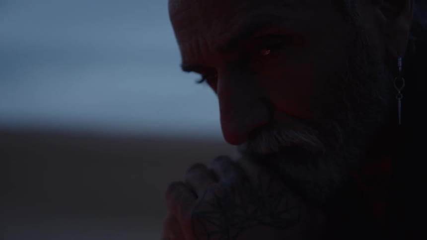 Man with gray hair and beard lit by warm light in a dark outdoor setting