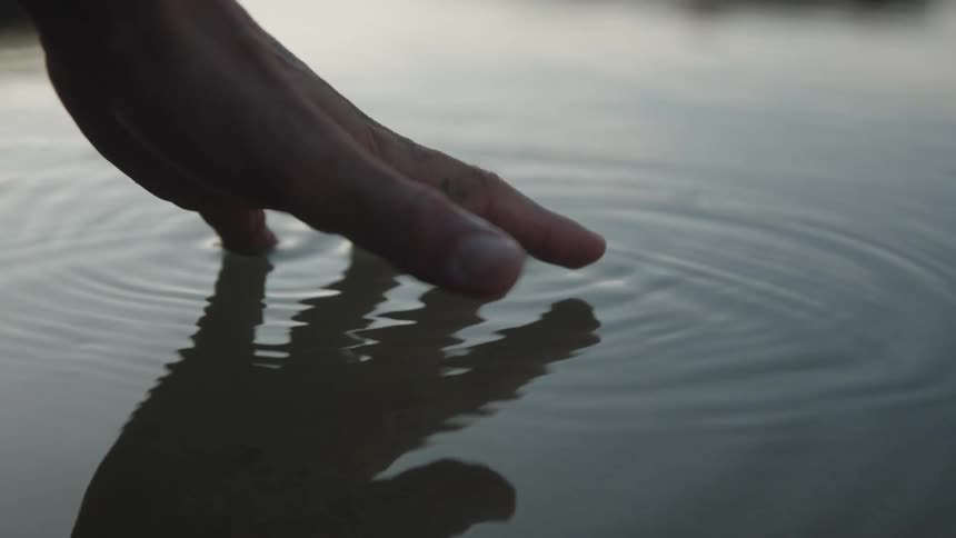 Hand touching the water surface and creating small ripples