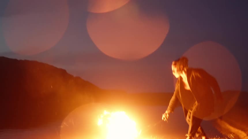 An older man with long tied hair holding a branch thats on fire then dragging it along the ground