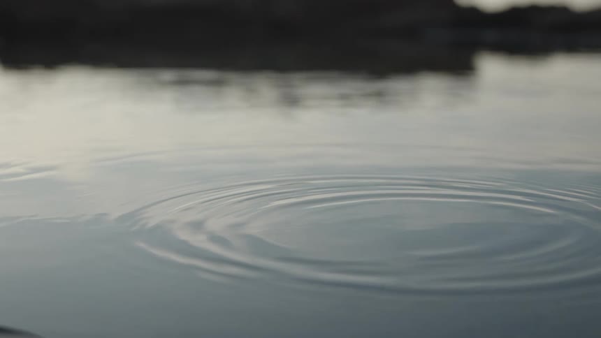 Water droplets hit the water on a lake near a large rock formation