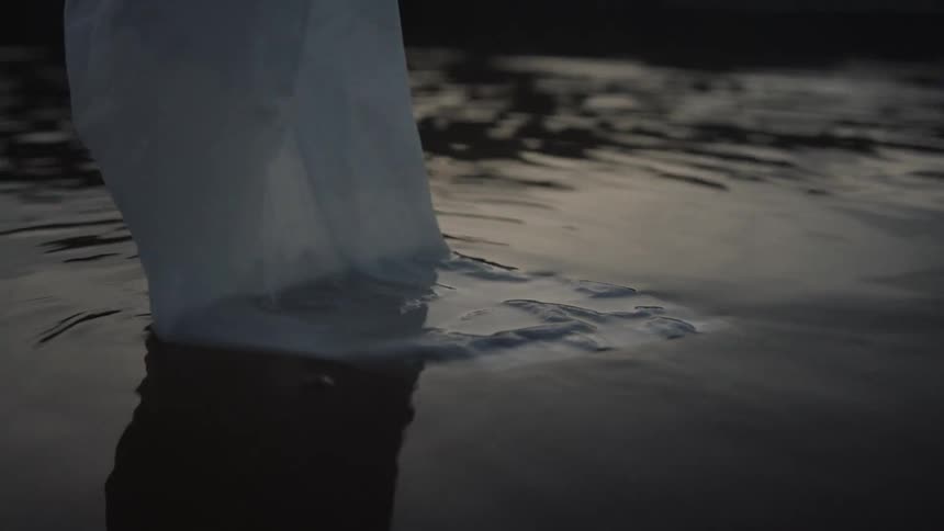 A close view of a white cloth dragging in the shallow dark water creating ripples on the wet reflective surface