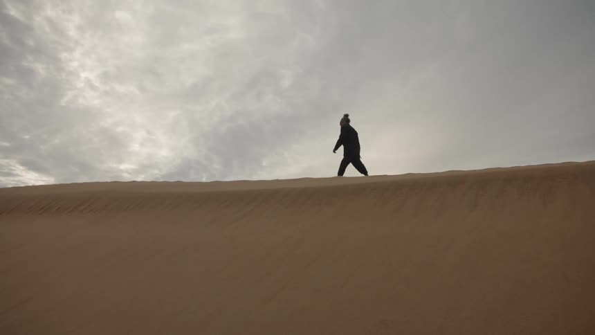 A young man walking across a sand dune in a desert during daytime
