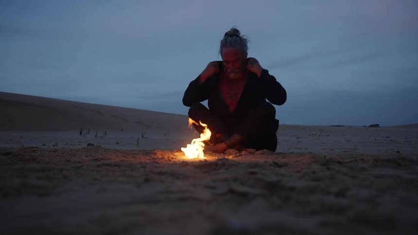 The man sits by a flame on the beach