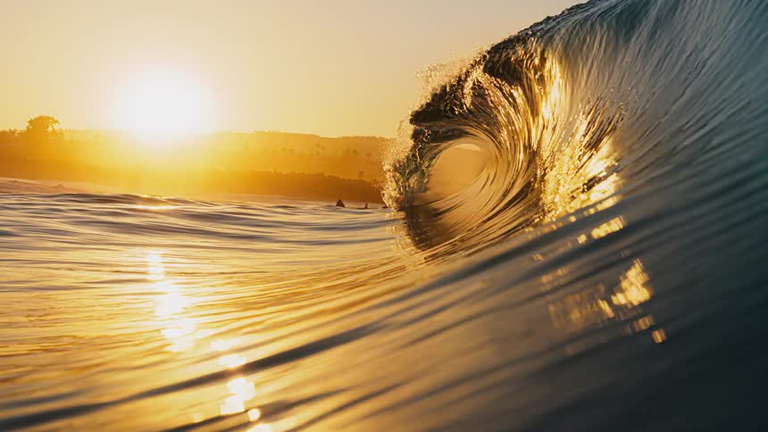 Golden wave curls into tunnel at sunset with reflections on the water