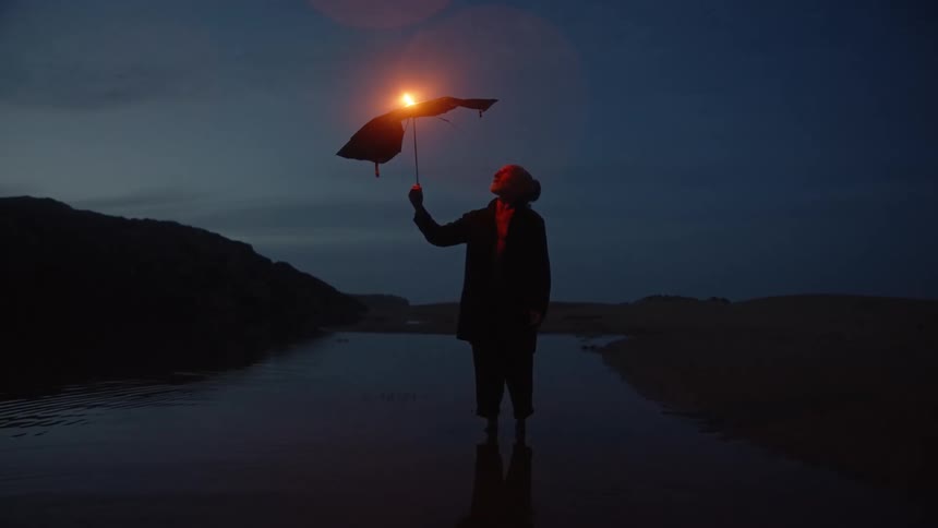 Person standing in shallow water holding burning umbrella against deep blue sky