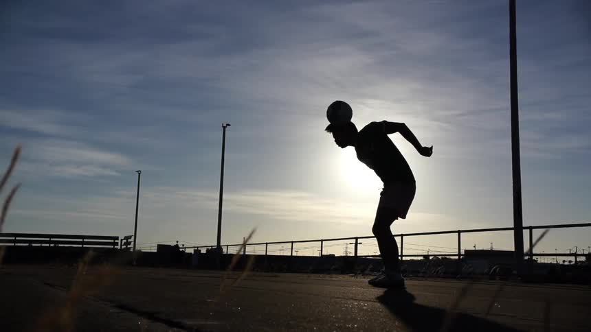 A young man rolling a ball up and over his back, over his head, standing up and catching it under a cloudy sky