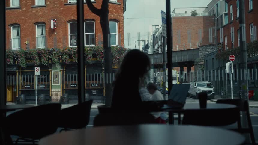 Silhouetted woman working on a laptop by a cafe window