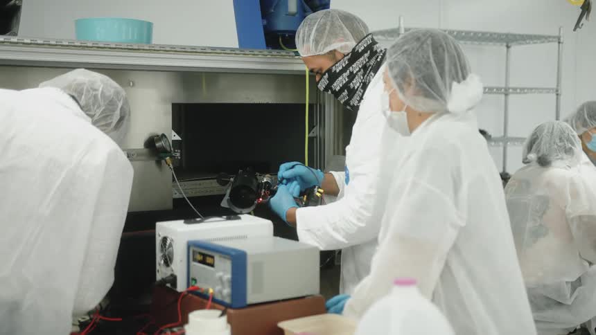People in a lab wearing white suits working on an experiment