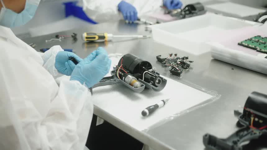 A worker assembles electronic machinery on a stainless steel tabletop in a lab
