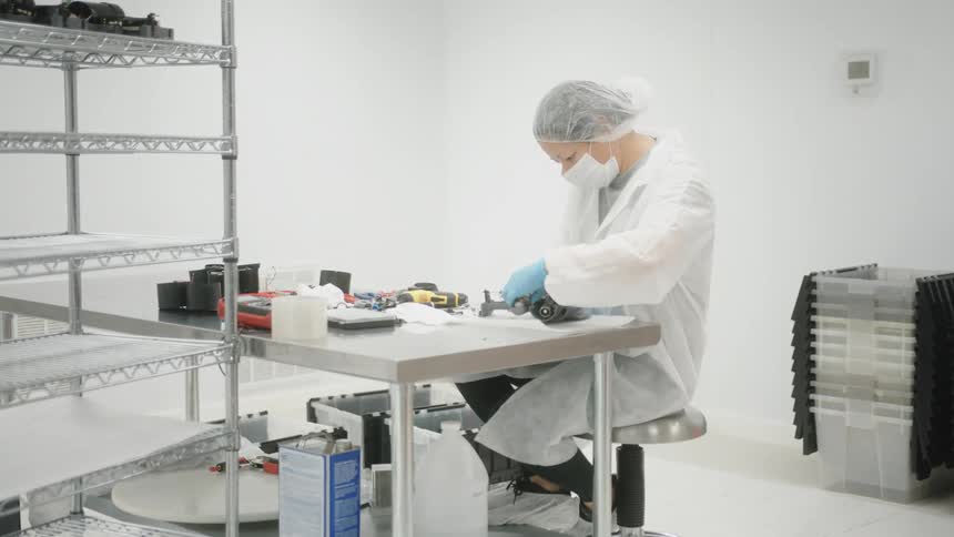 Technician assembling a device on a stainless steel workbench in a cleanroom