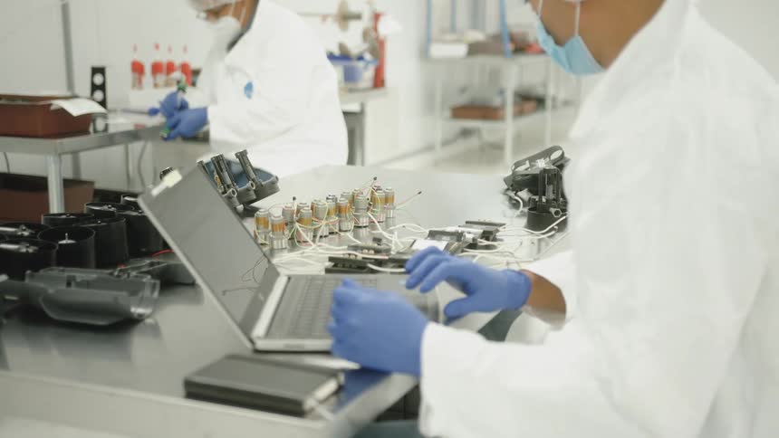 Two professionals in a controlled environment operating electronic devices on a stainless steel bench