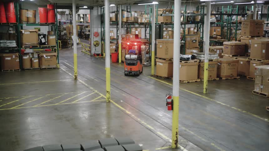 Worker driving forklift to load cardboard boxes in a warehouse