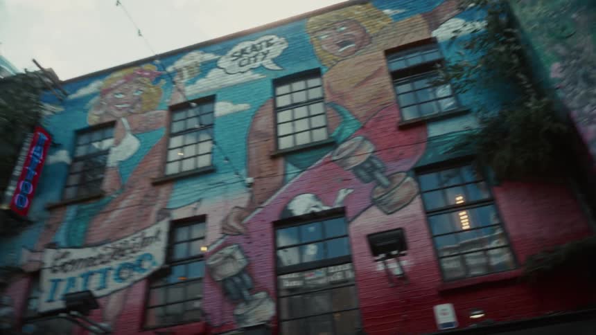Vines grow up the outside of mural covered shops on a summer day