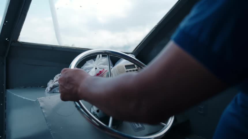 The video is an interior shot of a small boat cabin or enclosure from the perspective of the passenger side a persons hands are visible on the chrome steering wheel next to a dashboard with gauges