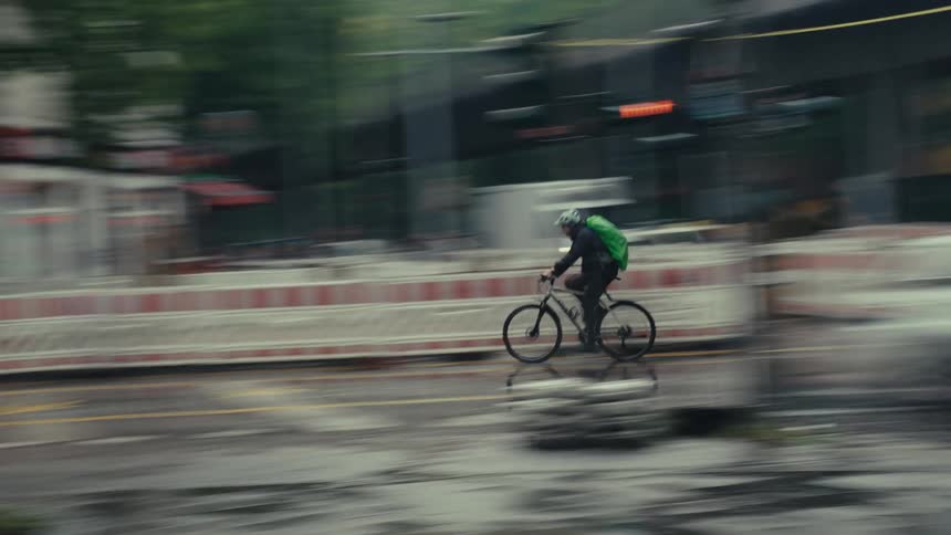 A person rides a bicycle quickly on a wet city street becoming the sharp focus against a background that blurs with motion passing by cars and white road dividers (slow shutter)