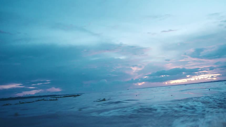 The video is an extreme long shot showing waves of dark blue water and a sky filled with dramatic dark grey and blue storm clouds the horizon is a faint band of light where the clouds part slightly