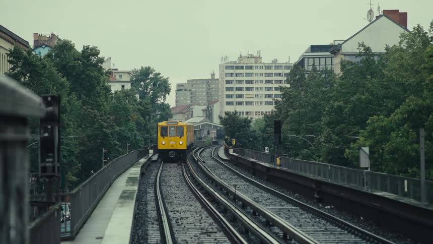 Yellow subway train moving on elevated track amid trees and buildings