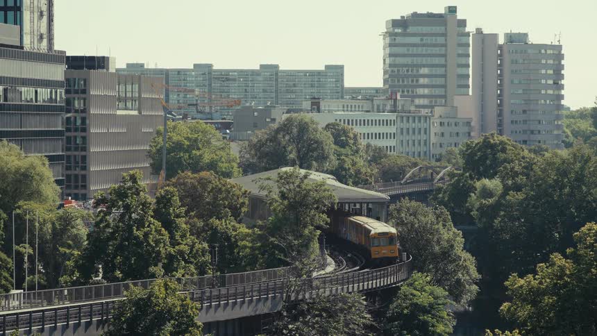 A public train moves on an elevated track into a covered stop in a city