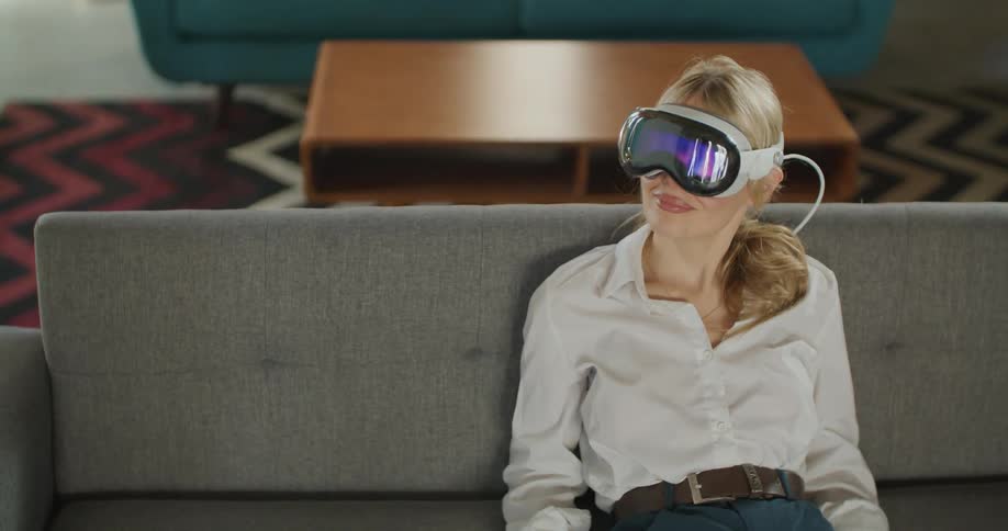 Woman wearing vr headset sits on gray couch in office