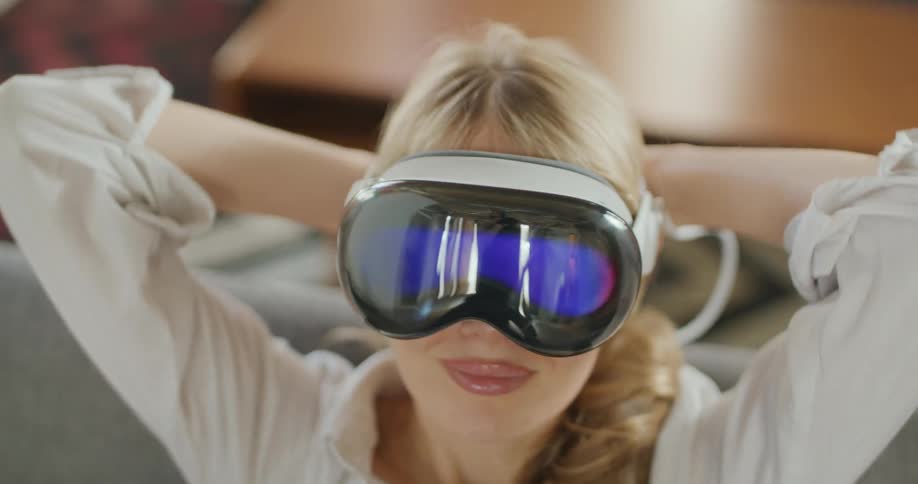 A blonde woman sitting on a couch wearing a virtual reality headset