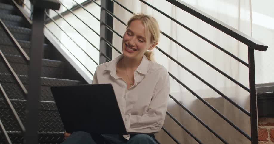 A woman sitting on stairs is looking at a laptop and smiling and talking