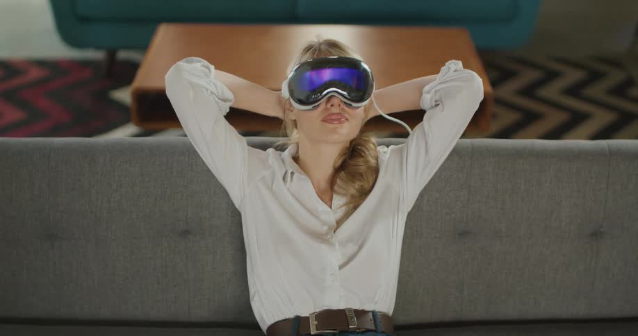 A blonde woman sitting on a couch wearing a virtual reality headset