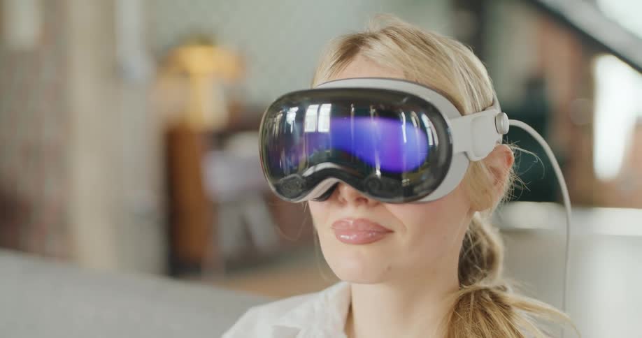 A close view of a smiling blond woman wearing a white shirt and a sleek gray virtual reality headset with mirrored lenses in an indoor setting