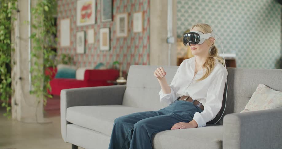 Young woman sitting on the couch wearing a virtual reality headset moving her hands