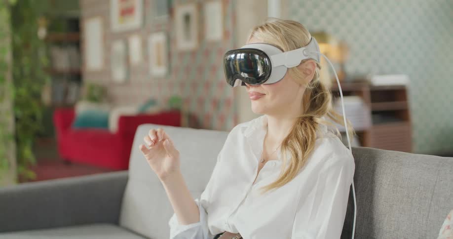 A blonde woman sitting on a couch playing a video game while wearing a virtual reality headset