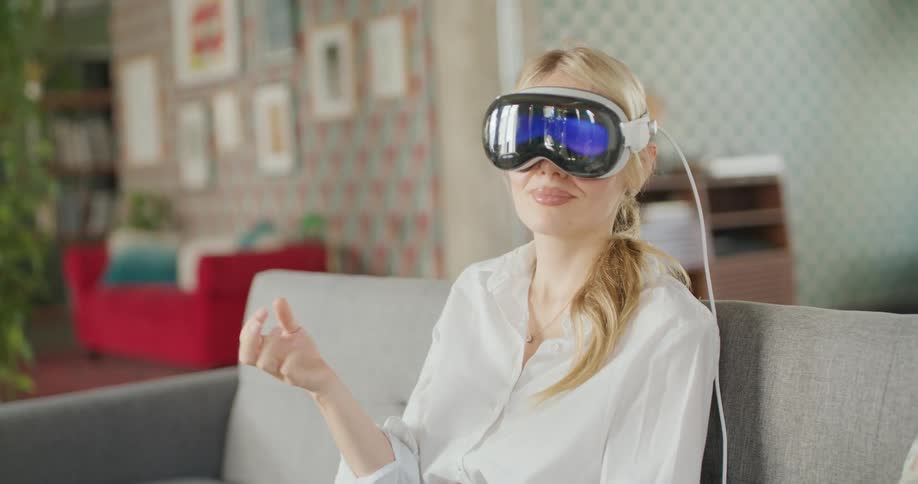 Young woman sitting on the couch wearing a virtual reality headset moving her hand