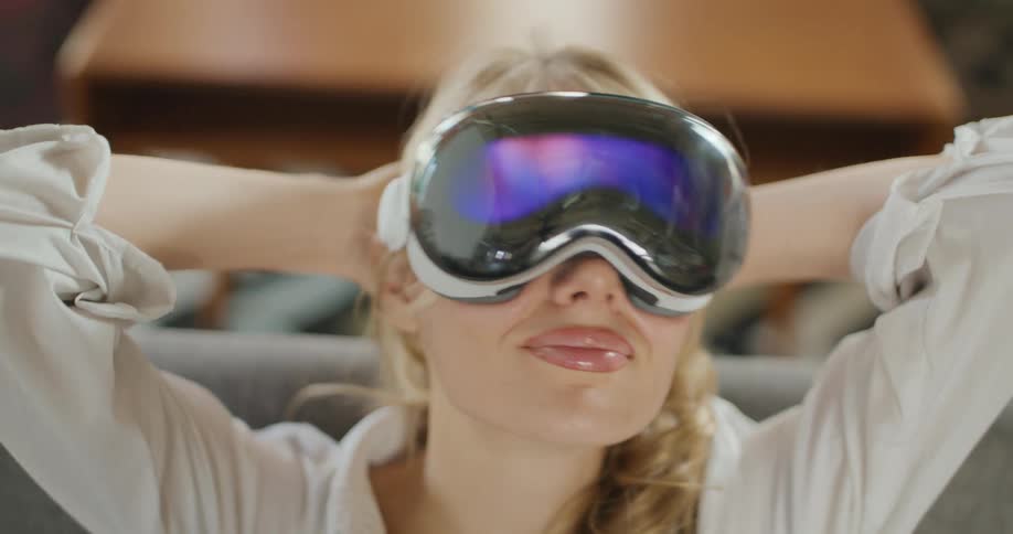 Young woman sitting on the couch wearing an apple vision pro headset smiles with her hands behind her head