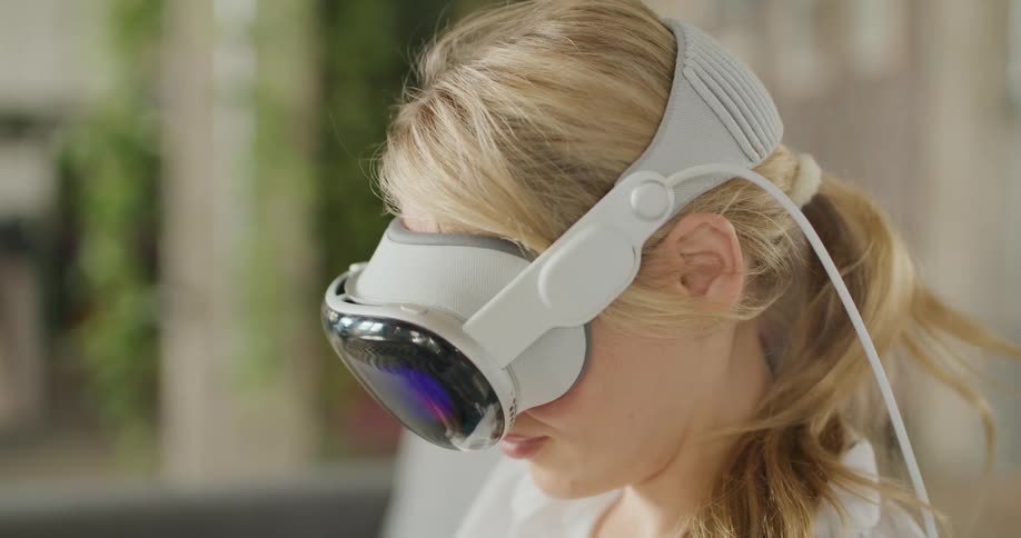 A woman wears a large glossy vr headset indoors lips slightly parted
