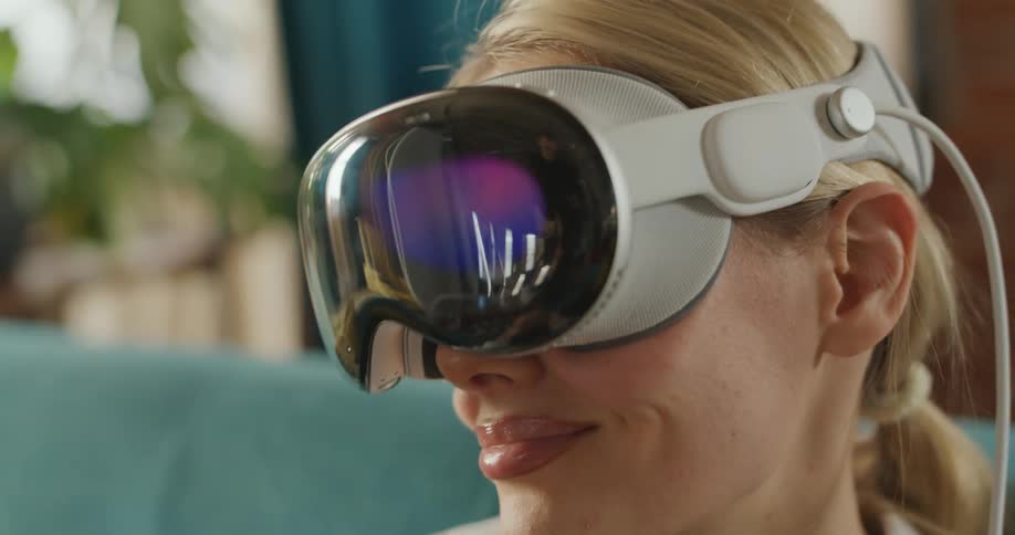 A woman putting on a white and dark visor virtual reality VR headset adjusting the device on her head then smiling as a blue and purple light glows on the reflective surface of the visor
