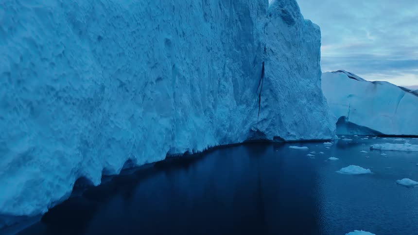 Massive blue iceberg in dark ocean with floating ice under overcast sky