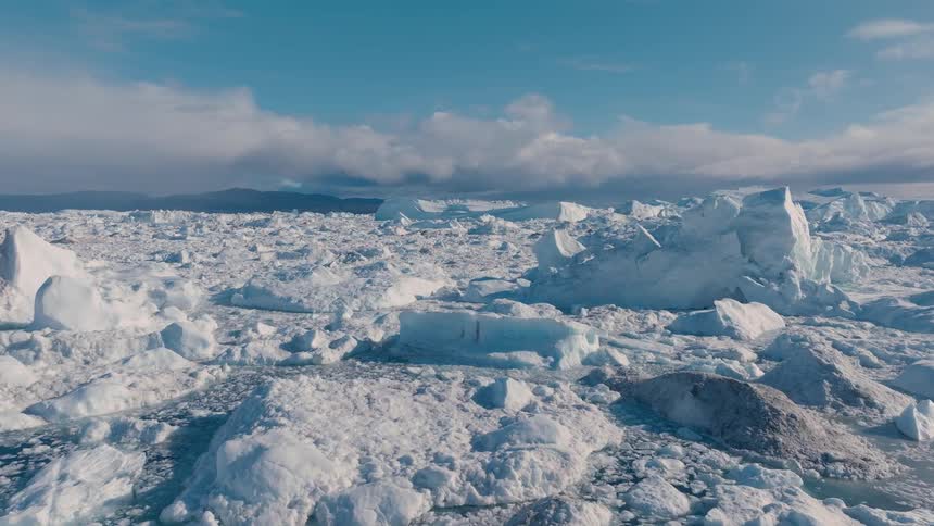 Aerial view of icebergs floating in icy blue water under a partially cloudy sky