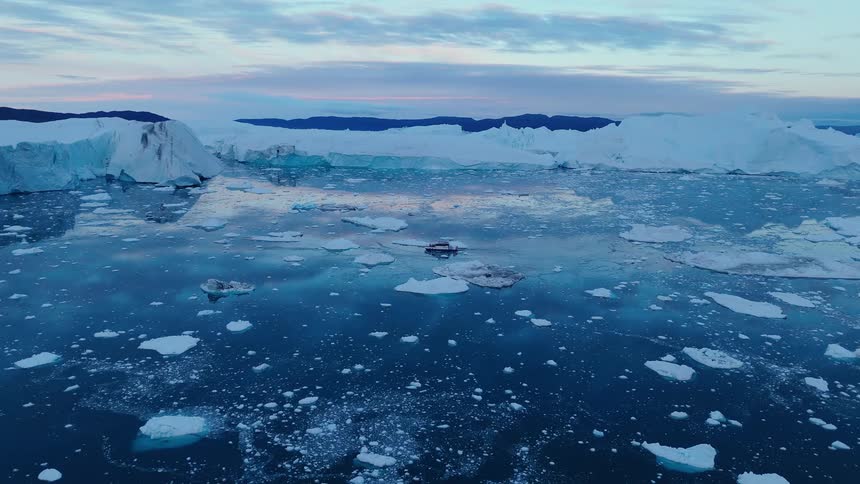 A wide icescape of bright glaciers borders a dark winding channel under patchy clouds