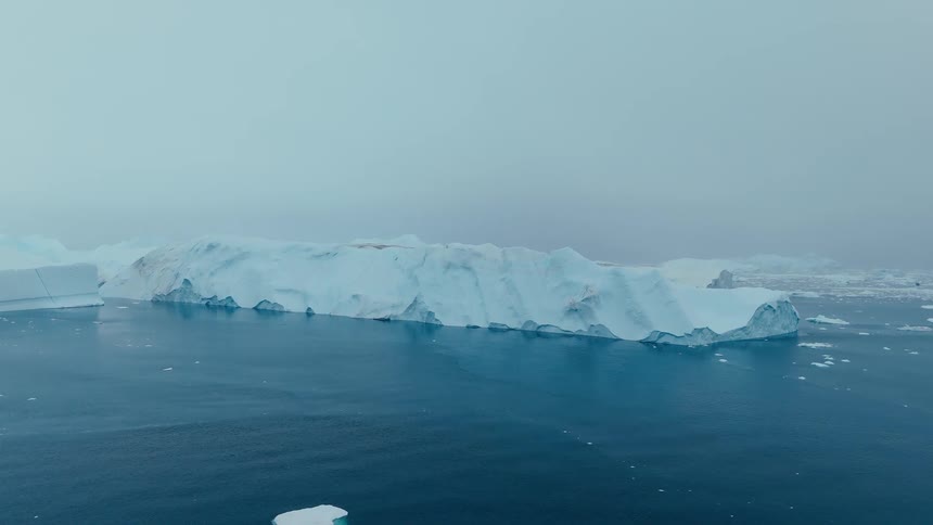 Aerial view of a lone ship sailing toward a massive iceberg in icy waters
