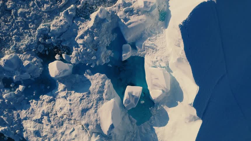 A narrow channel of deep blue water separates two fields of white ice and large chunks of ice float and line the edges of the water passage