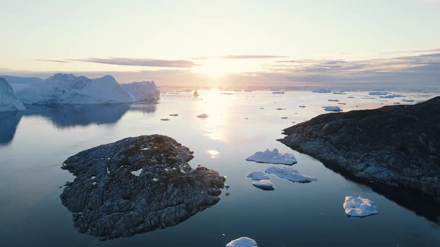 Red sailboat sailing among icebergs under sunset sky