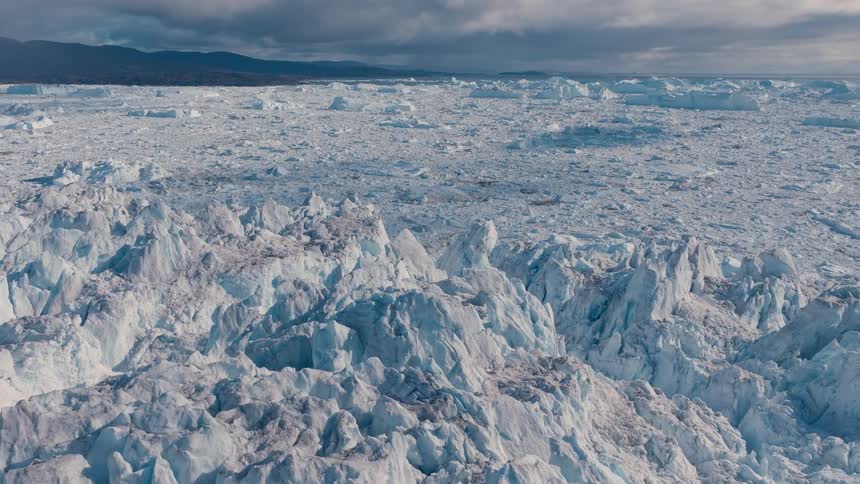 Aerial view of jagged glacier ice and icebergs under a cloudy sky