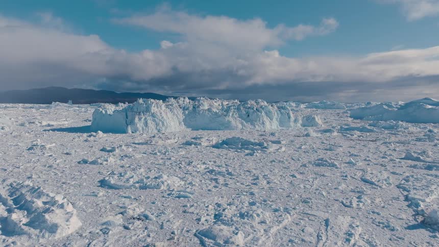 Aerial view of sea ice and icebergs near rocky coastline under sky