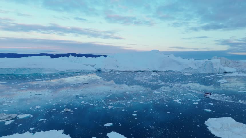 Aerial view of boat navigating icy sea with icebergs at dusk