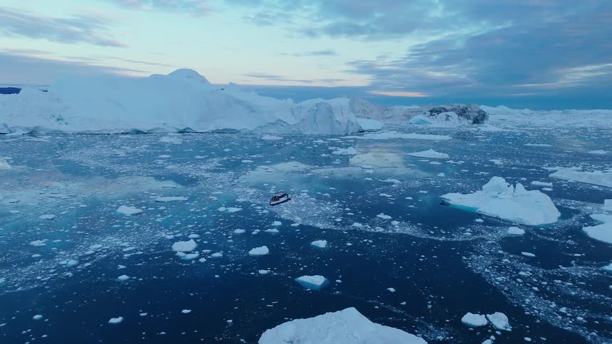 Aerial view of a boat among icebergs in the arctic ocean at twilight