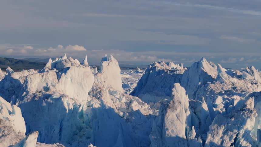 A sprawling field of jagged bluewhite ice peaks stretches toward a distant low horizon under a calm sky