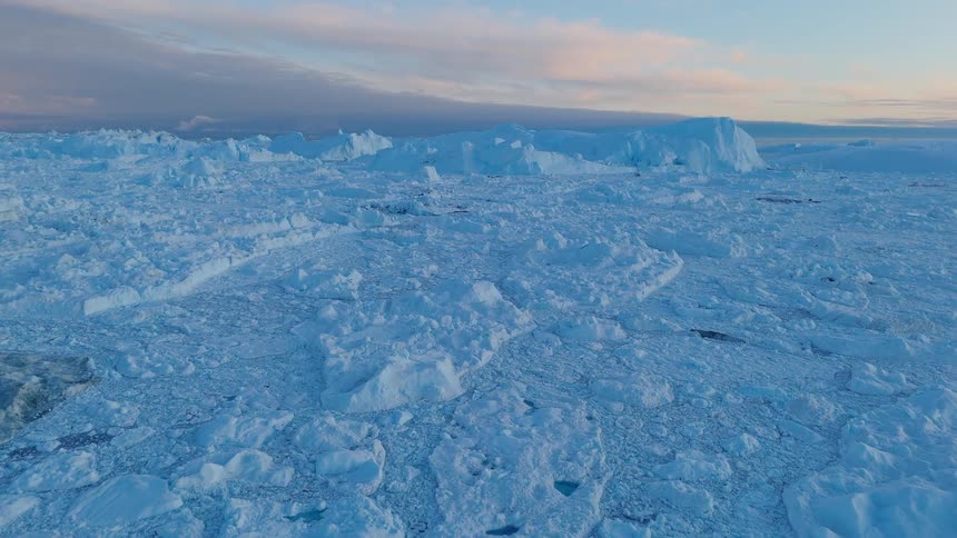 A wide plain of bluetinged sea ice and hummocks stretches toward a pastel horizon beneath soft clouds