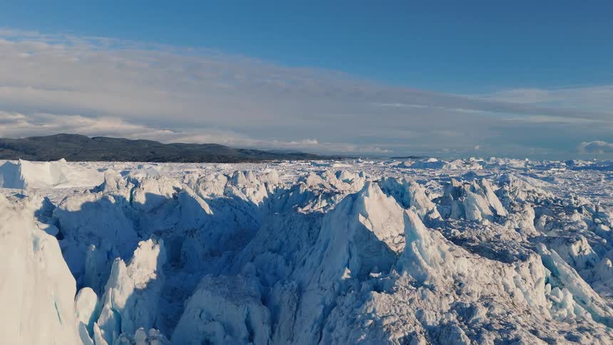 A massive textured wall of white and blue glacial ice rises dramatically beneath a clear bright blue sky in the arctic
