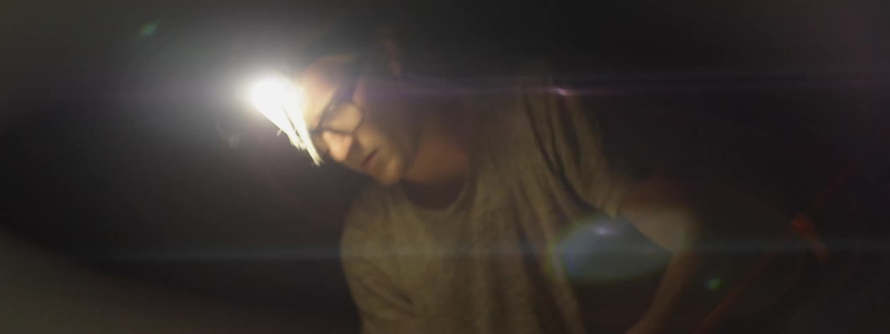 A man wears a headlamp while setting up a tent at night