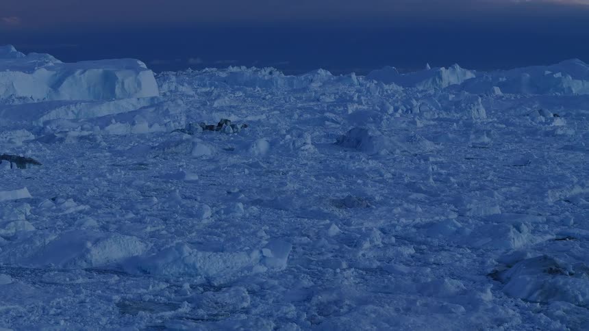 The video provides an expansive view of a vast ice sheet or glacier under a dark twilight sky the foreground is densely covered with chunky bluetinged broken ice and rubble